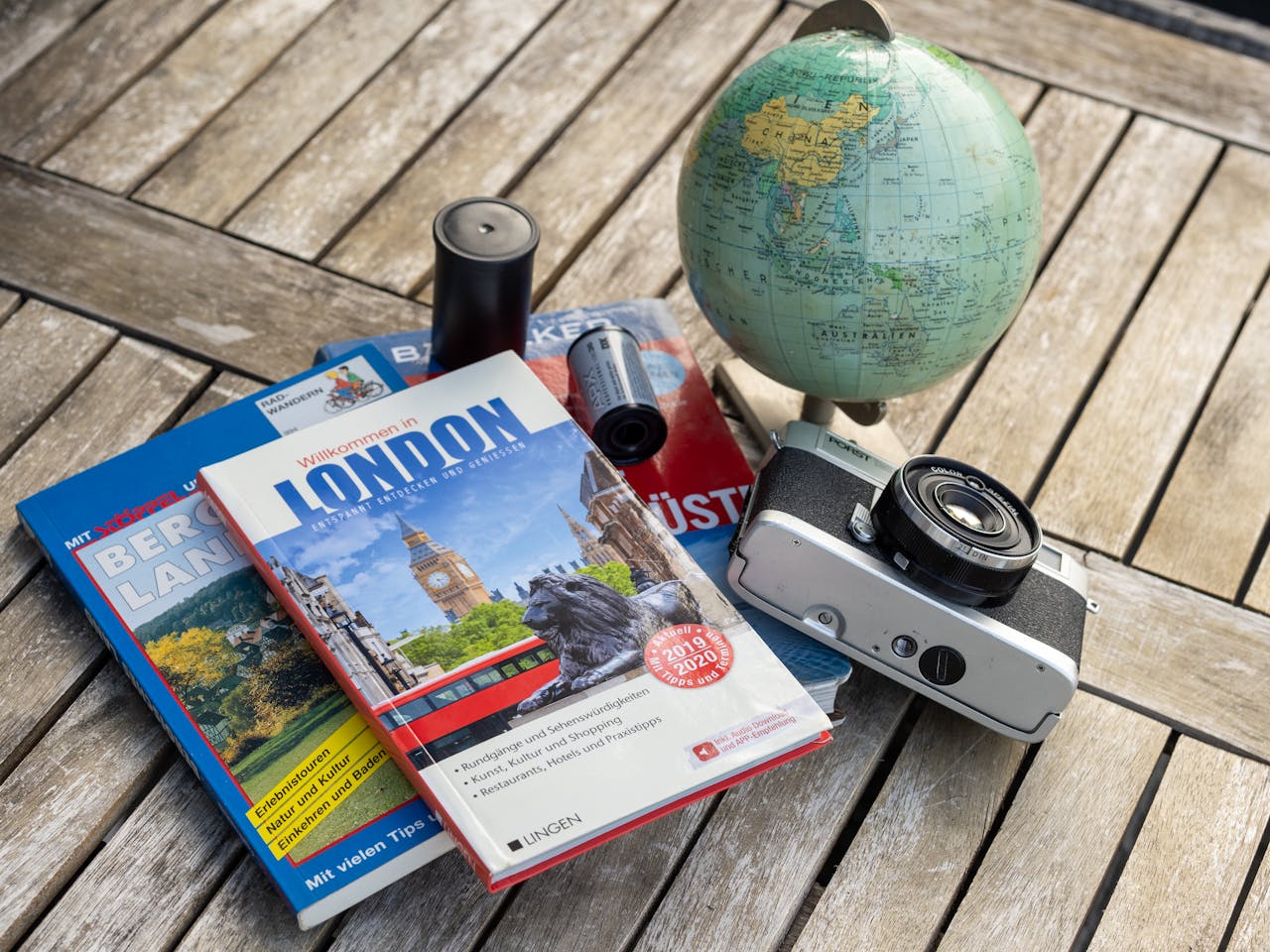 A vintage travel setup with guidebooks, a globe, and a film camera on a wooden table.